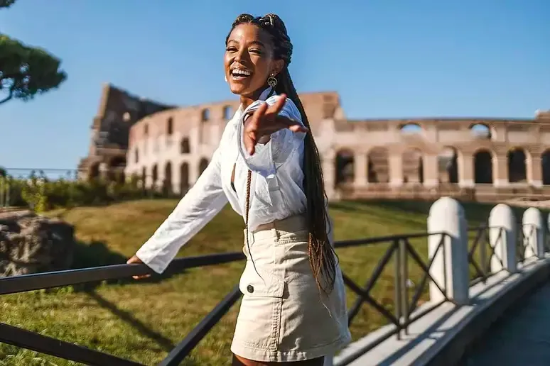 Mulher sorrindo apoiada em uma grade, com o Coliseu ao fundo