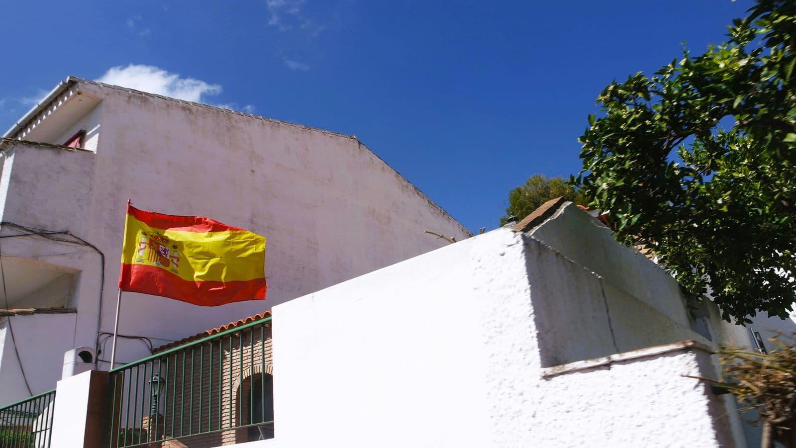 Bandeira da Espanha na parede de uma casa caiada de branco, ao lado de uma árvore