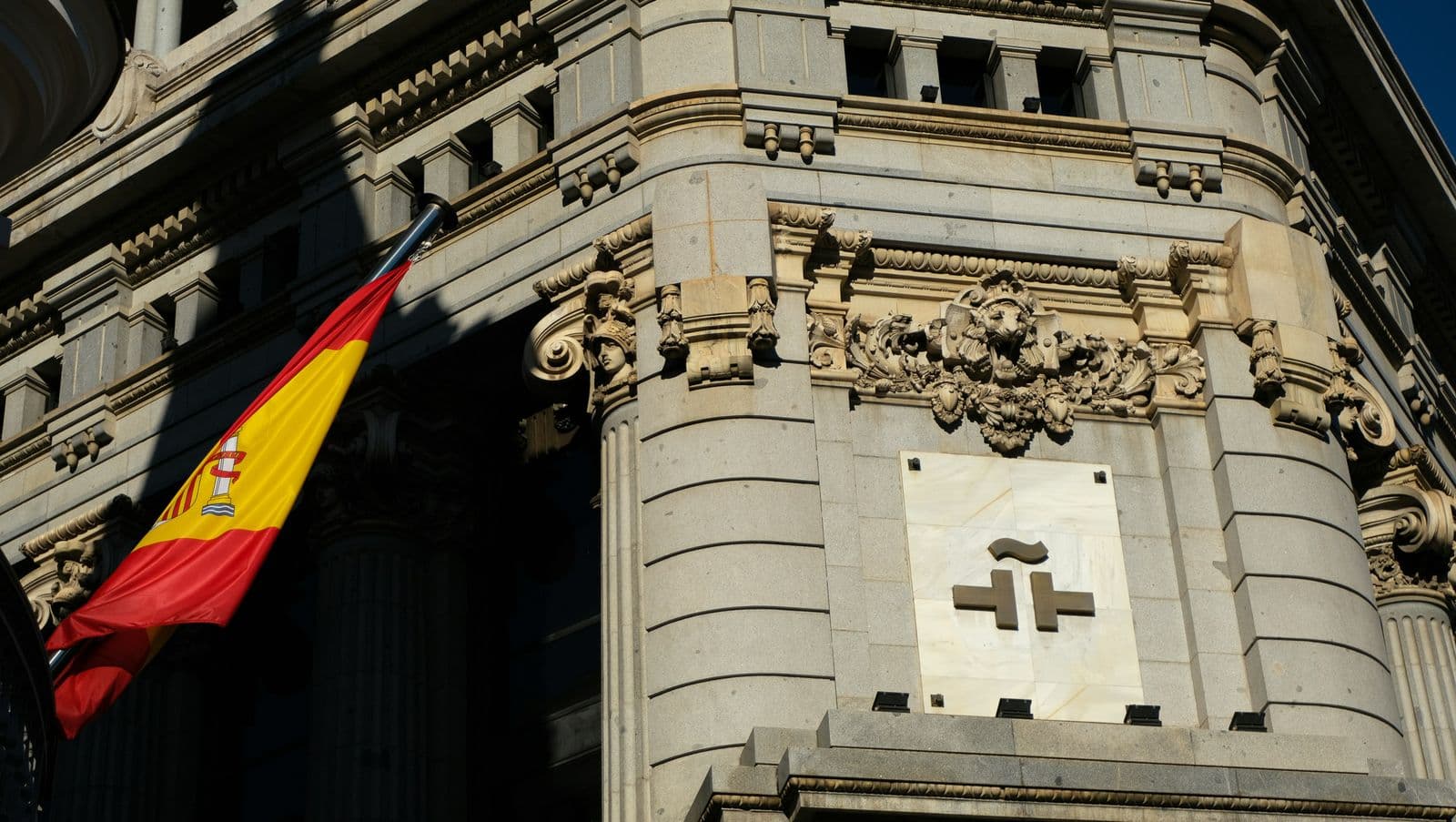 Bandeira da Espanha pendurada na fachada de pedra de um edifício institucional