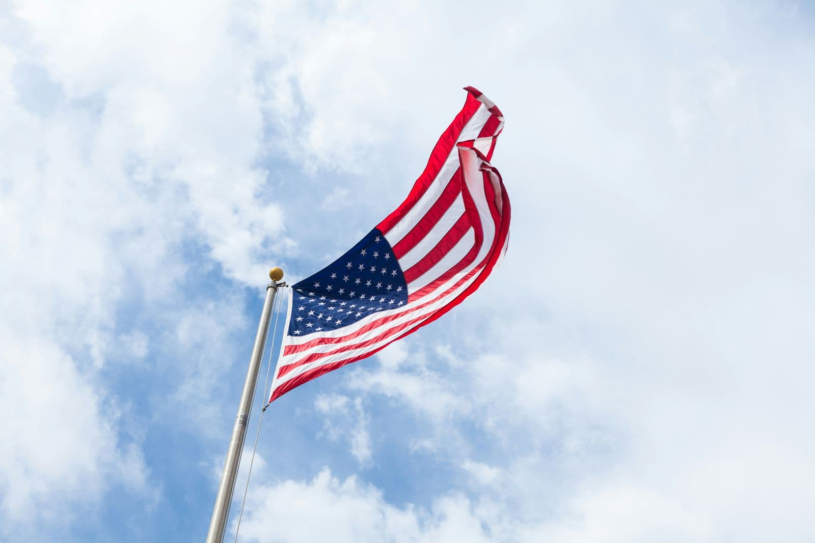Bandeira dos Estados Unidos no alto de um mastro, com nuvens ao fundo