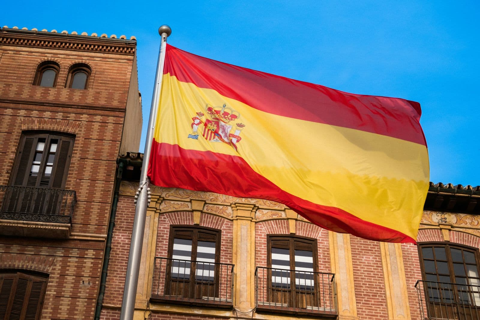 Bandeira da Espanha hasteada em frente à fachada de tijolos de um prédio antigo