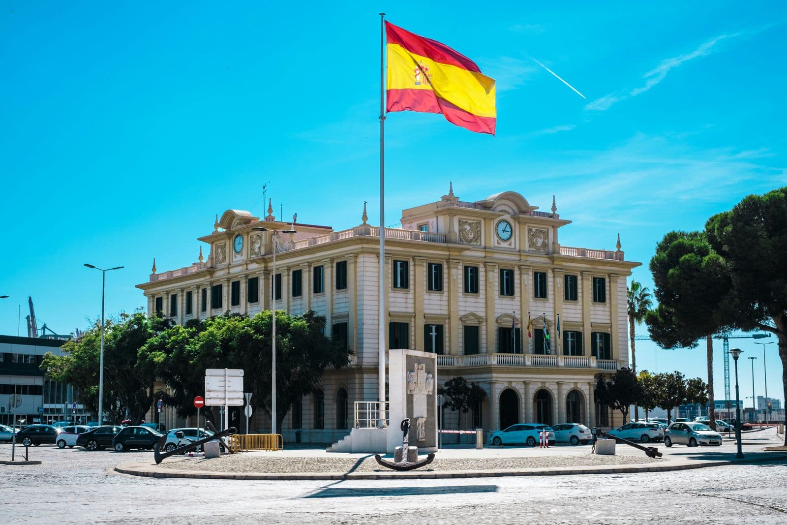 Bandeira da Espanha no alto de um edifício público de fachada clara, em uma praça