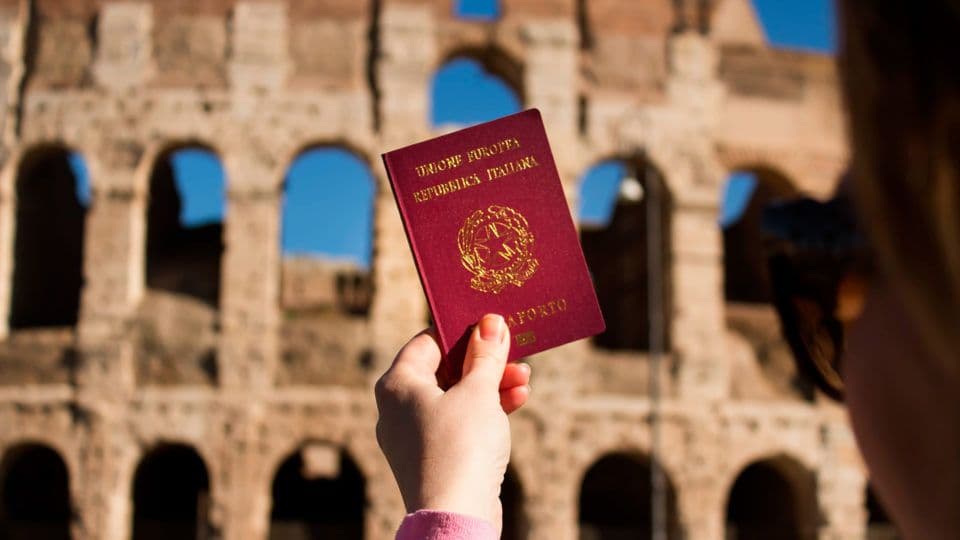 Mão segurando um passaporte italiano diante do Coliseu, em Roma