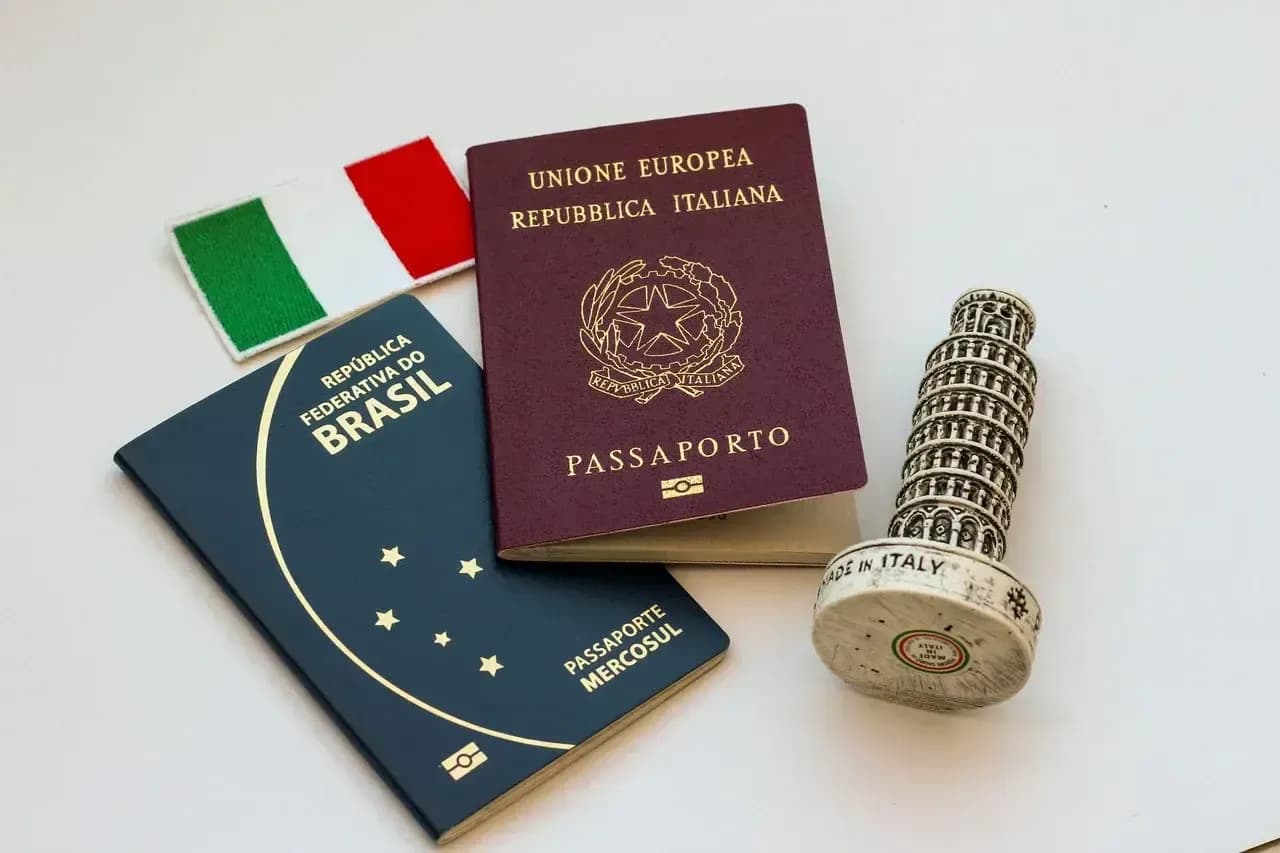 Passaporte brasileiro e passaporte italiano lado a lado, com uma miniatura da Torre de Pisa e uma bandeirinha da Itália