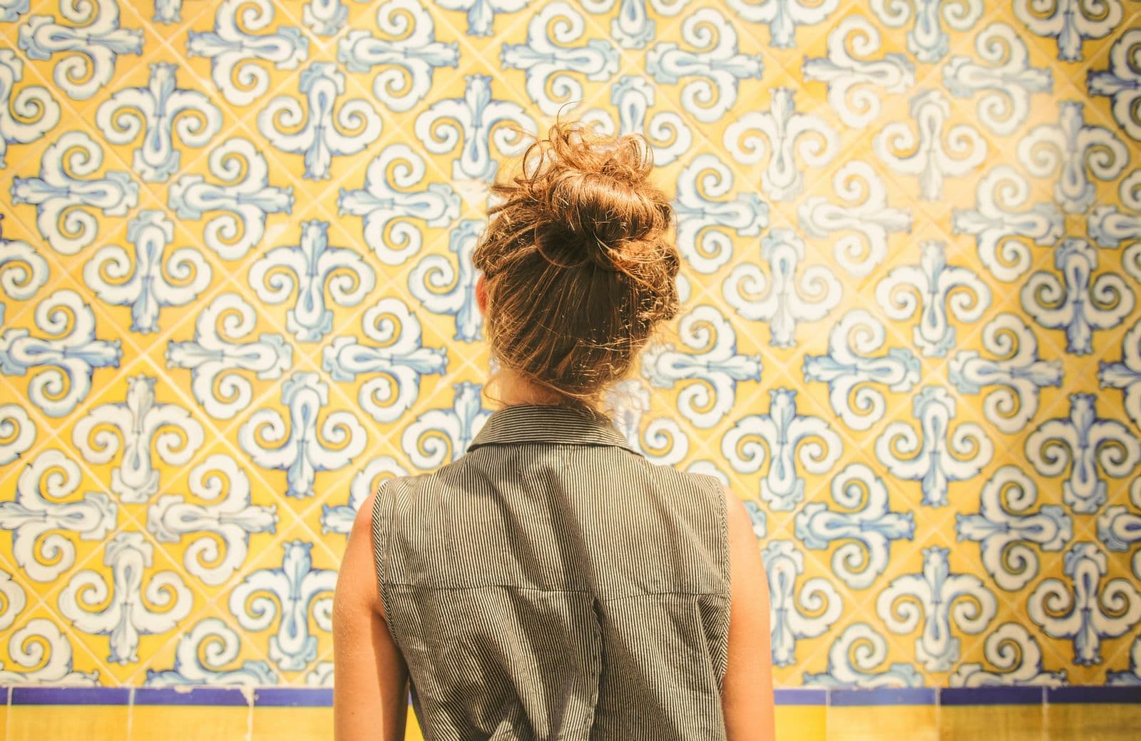 Mulher de costas diante de uma parede coberta de azulejos com desenho geométrico