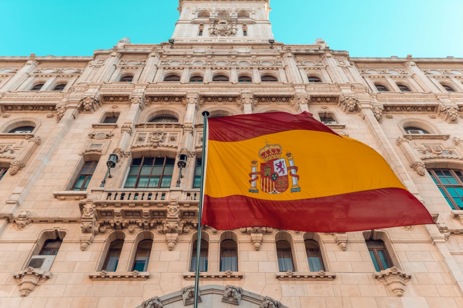 Bandeira da Espanha tremulando diante da fachada de pedra de um edifício histórico