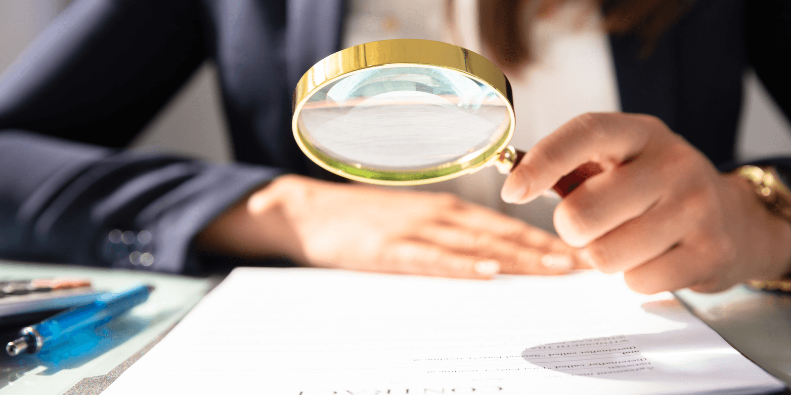 Mulher examinando um documento com uma lupa sobre a mesa