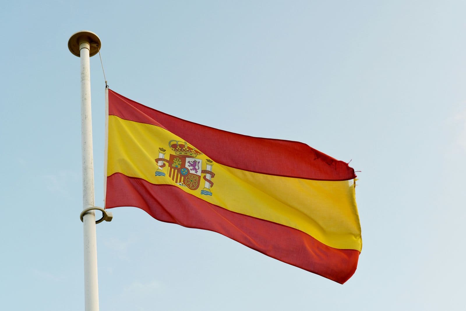 Bandeira da Espanha com o brasão nacional, hasteada em um mastro branco