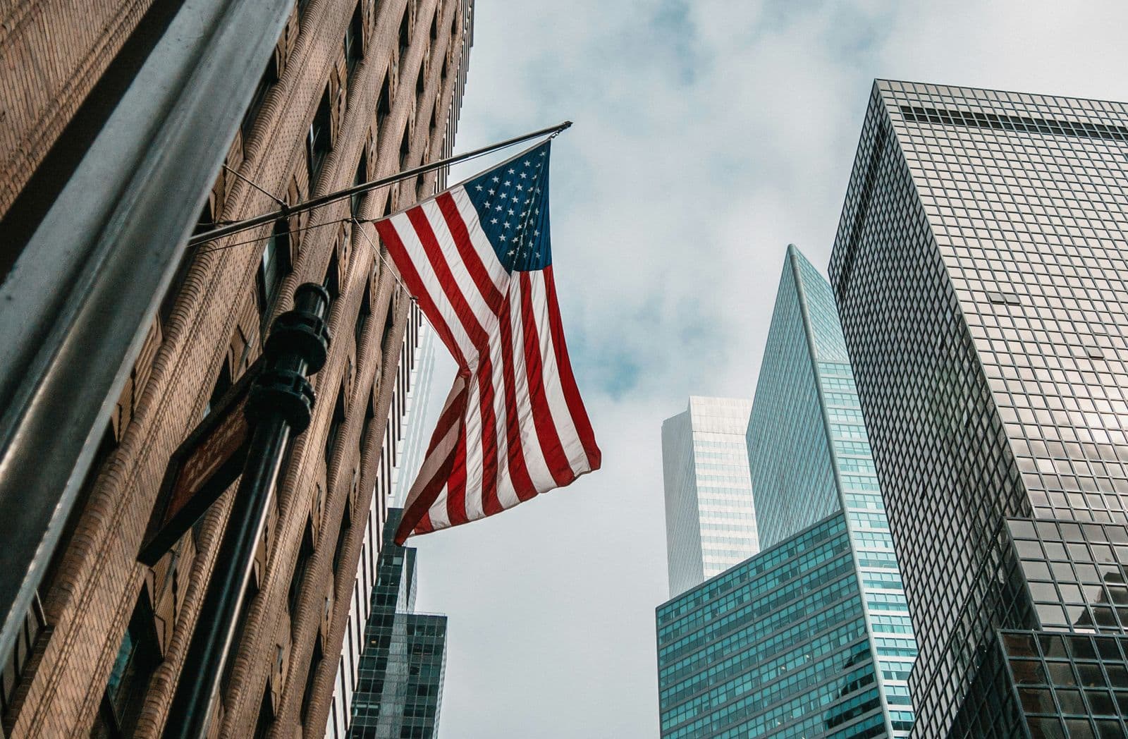 Bandeira dos Estados Unidos pendurada na fachada de um prédio, entre arranha-céus de vidro