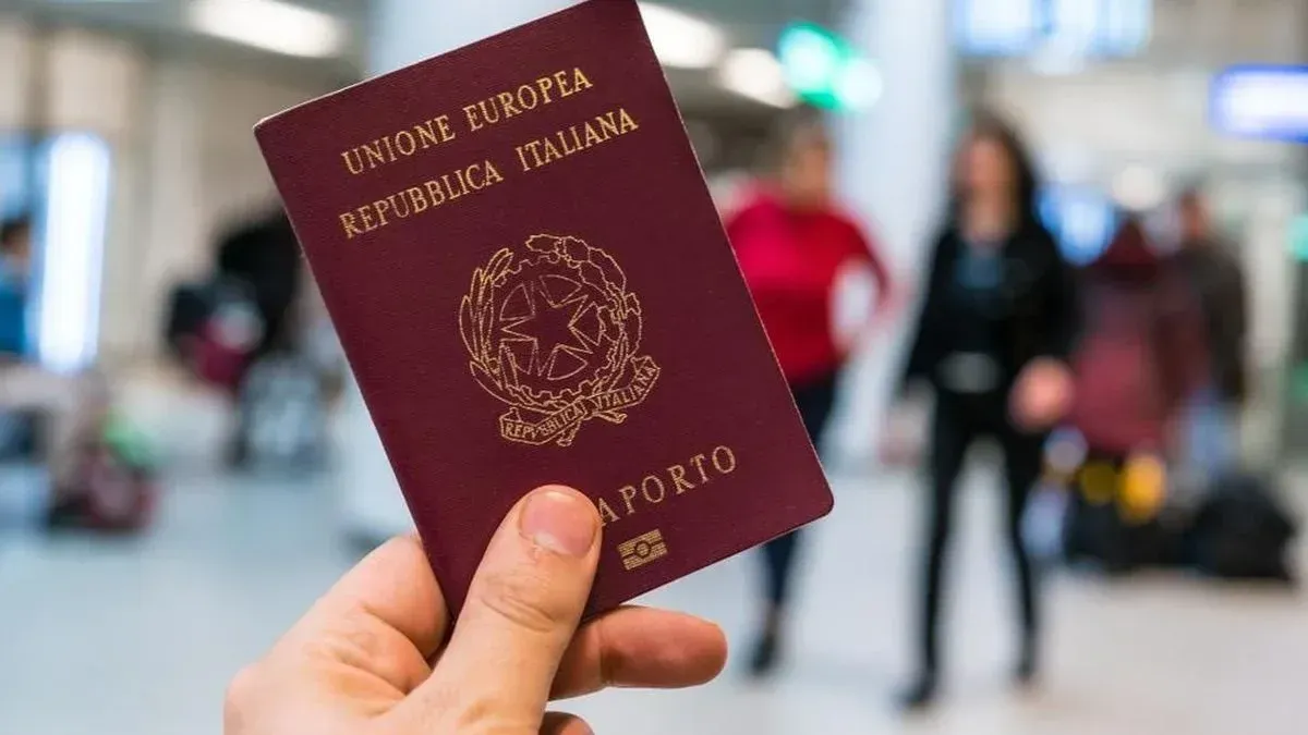 Mão segurando um passaporte italiano no saguão de um aeroporto