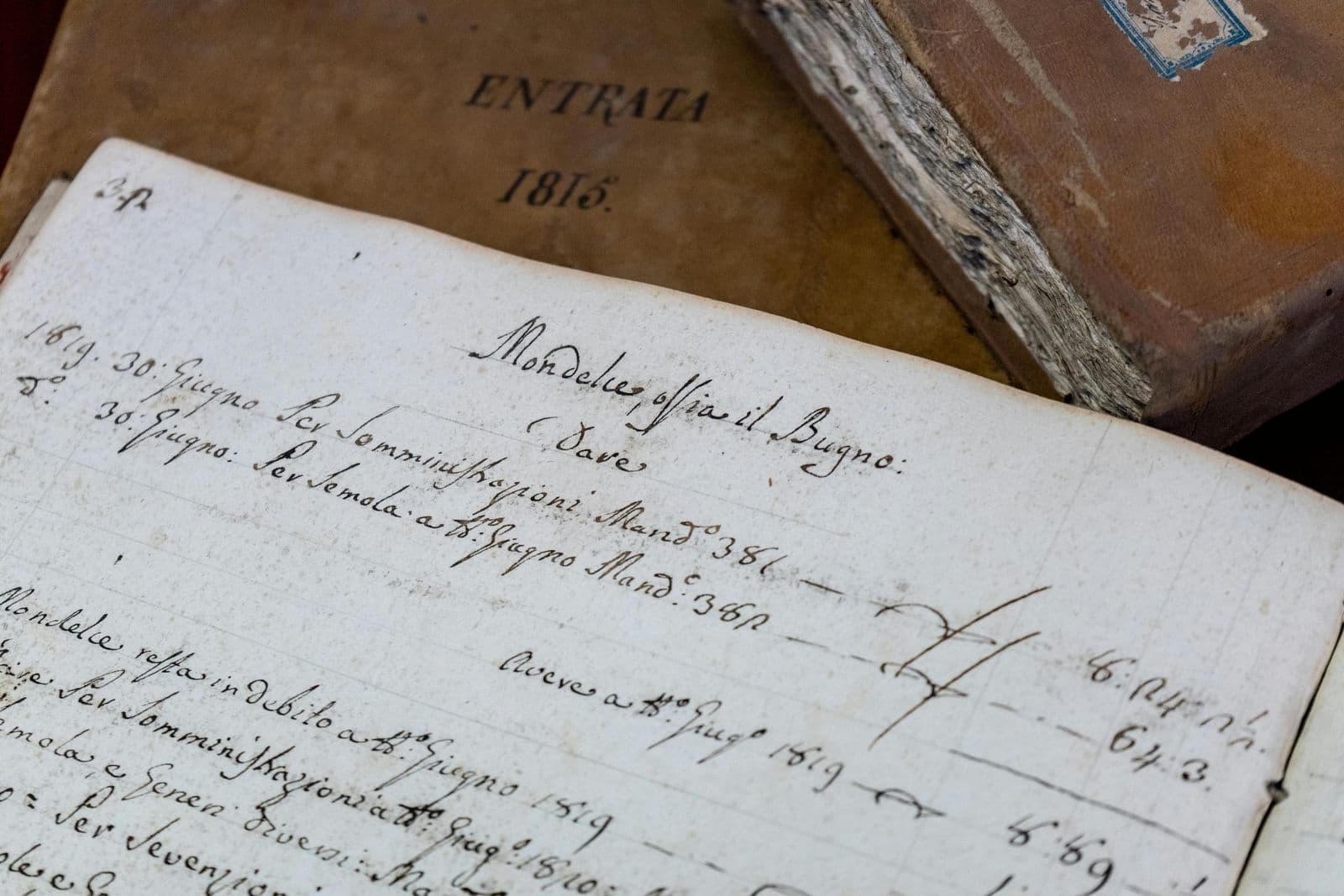 Livro de registro manuscrito de 1815, aberto, ao lado de um volume encadernado em couro