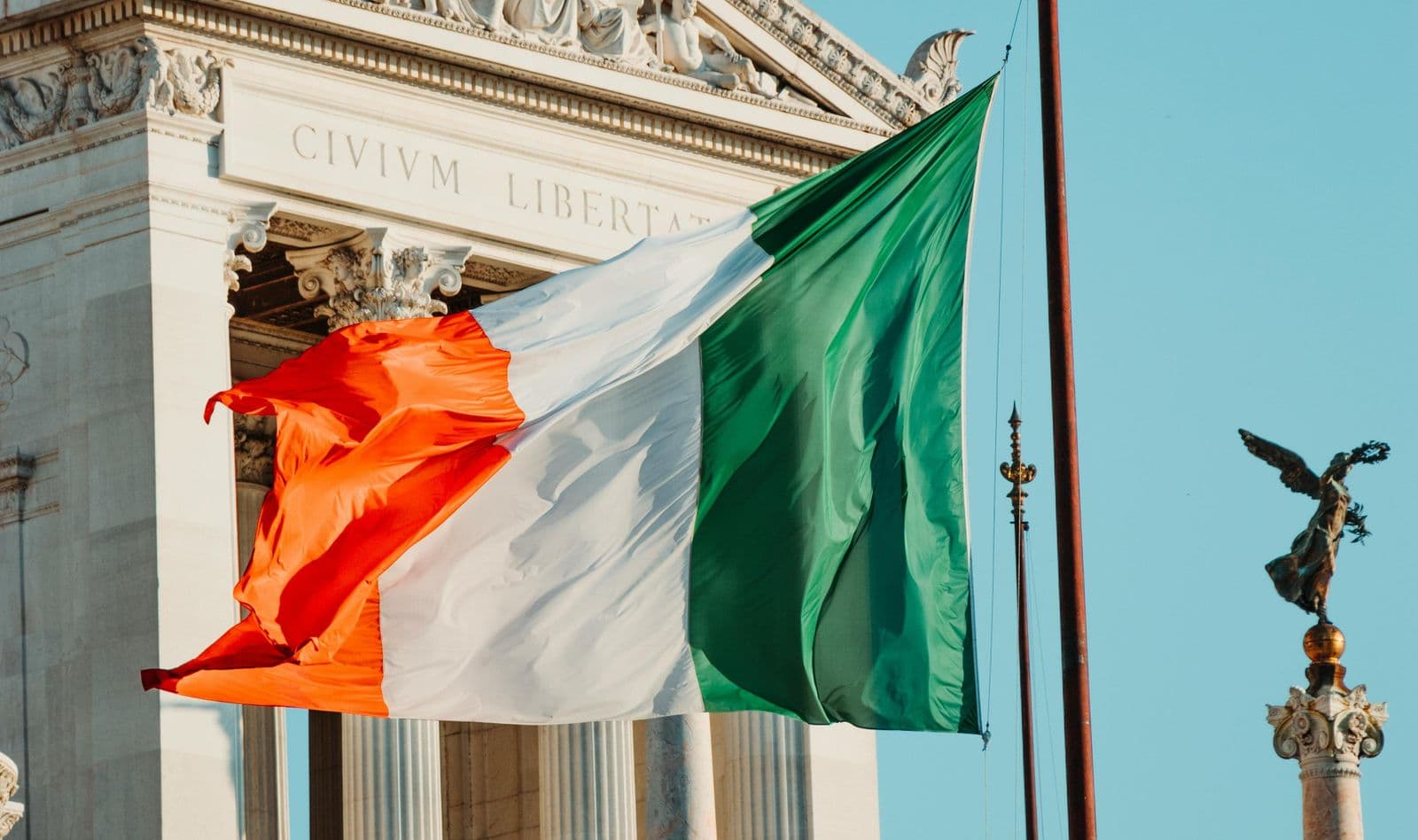 Bandeira da Itália tremulando diante da fachada de um edifício neoclássico em Roma