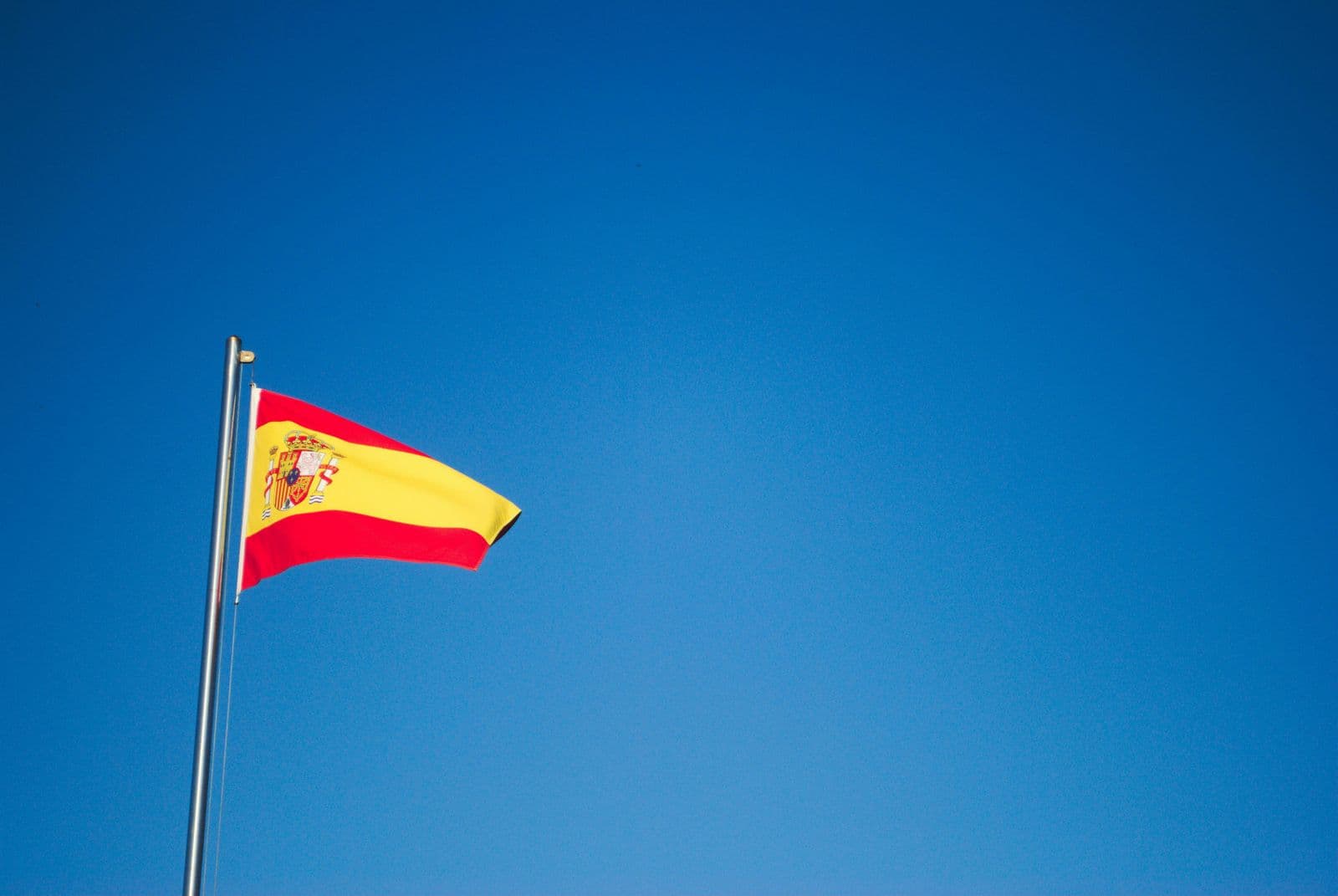 Bandeira da Espanha no alto de um mastro, contra o céu azul sem nuvens