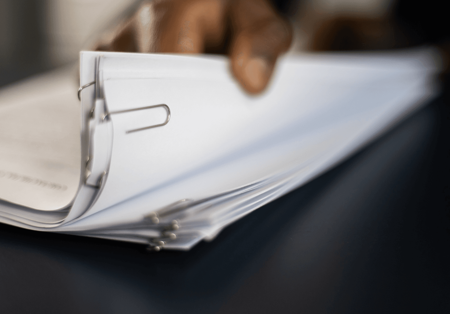 Mão folheando uma pilha de documentos presos por clipes